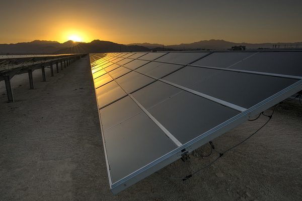 Solar panels in the desert, reflecting the sun behind mountains. 