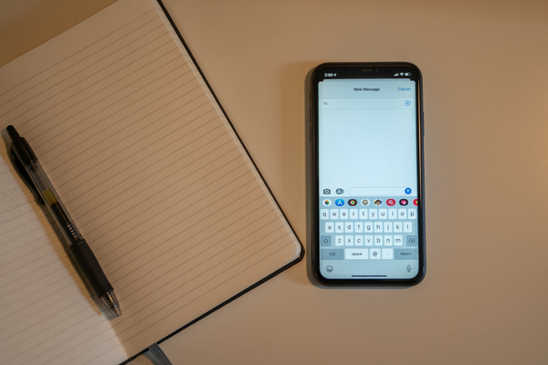 A blank notebook and a pen sit next to a mobile phone with a blank text message screen open. 